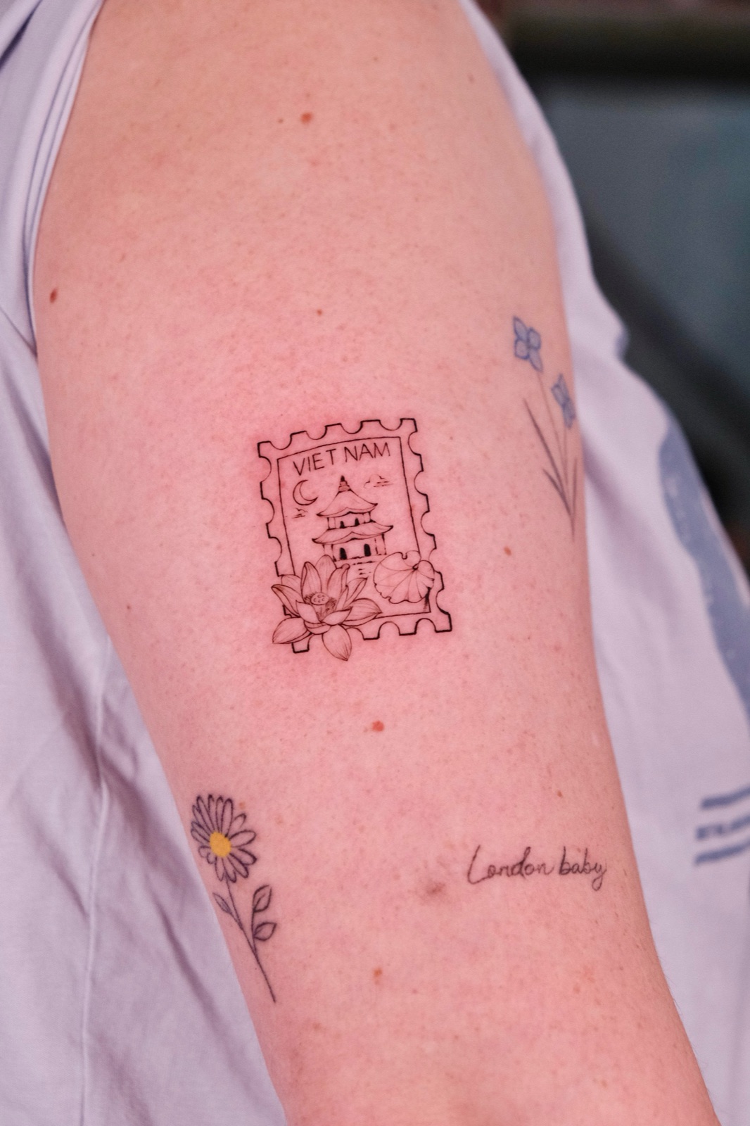 Fine-line Vietnam postage stamp tattoo with a pagoda, moon, and lotus flower, upper arm