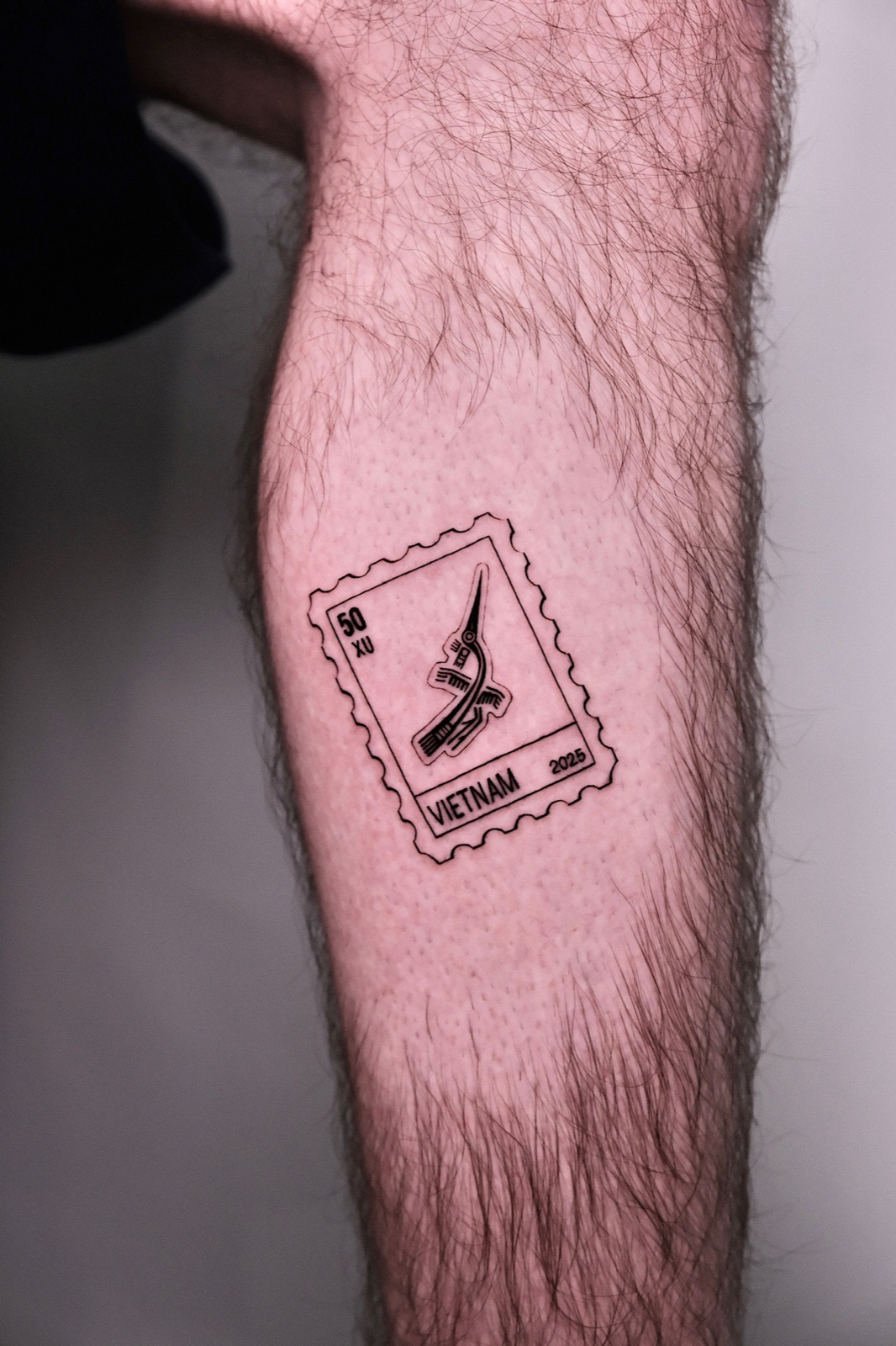 Forearm postage stamp tattoo with a tribal bird motif, fine black line