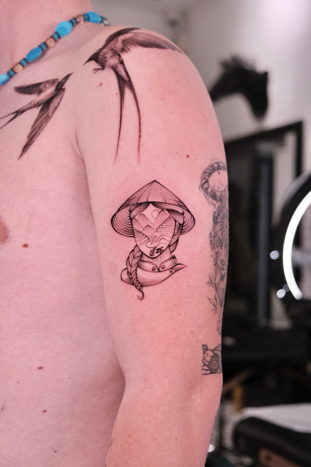 Fine-line tattoo of a woman in a Vietnamese conical hat with a mountain landscape design inside her face, on the upper arm