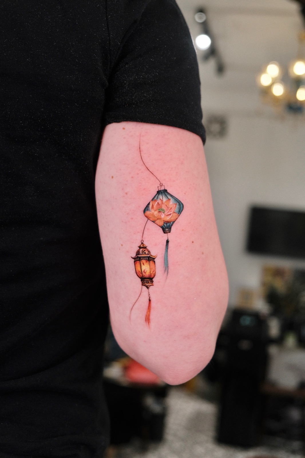 Colorful tattoo of hanging Vietnamese lanterns with a lotus flower on the forearm