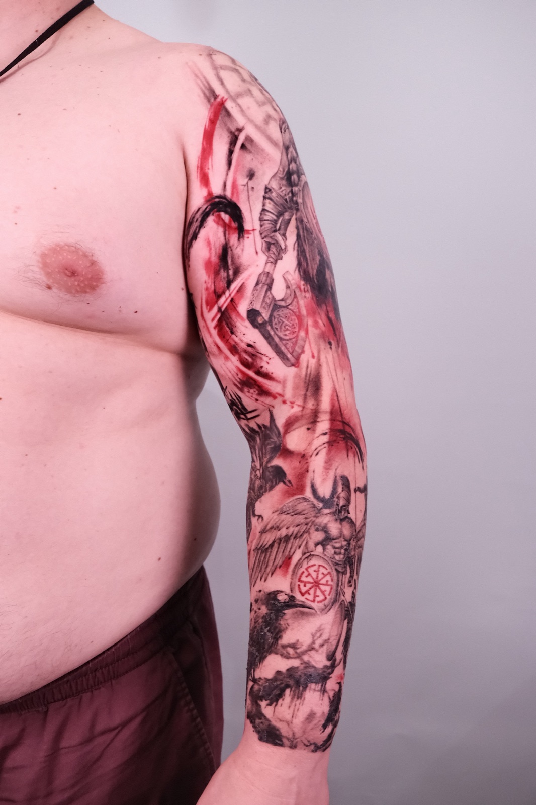Full sleeve tattoo of a Viking warrior with a raven, shown mid black-and-grey shading