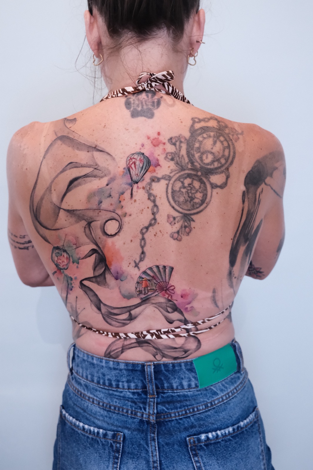 Watercolor-style full back tattoo collage combining pocket watches, a balloon, chains, and a figure in a conical hat