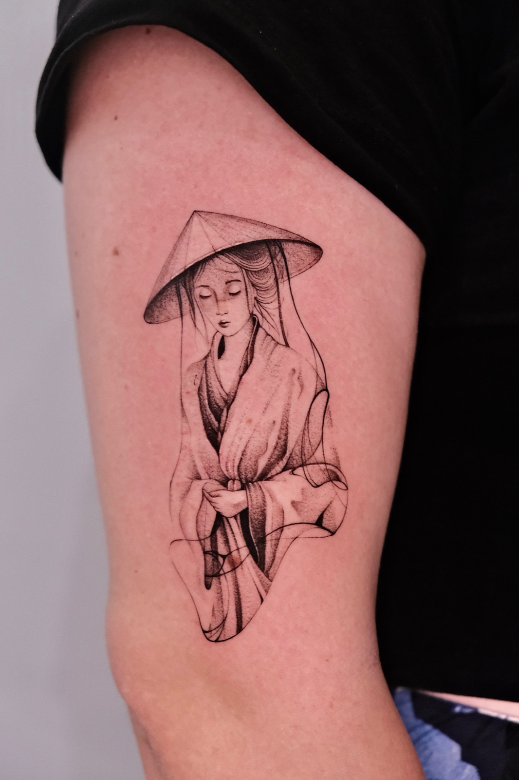 Upper arm portrait tattoo of a woman wearing a traditional conical hat