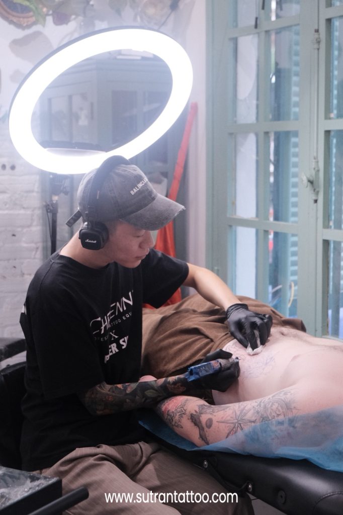 Sutran artist working slow, steady linework during a client's first tattoo session