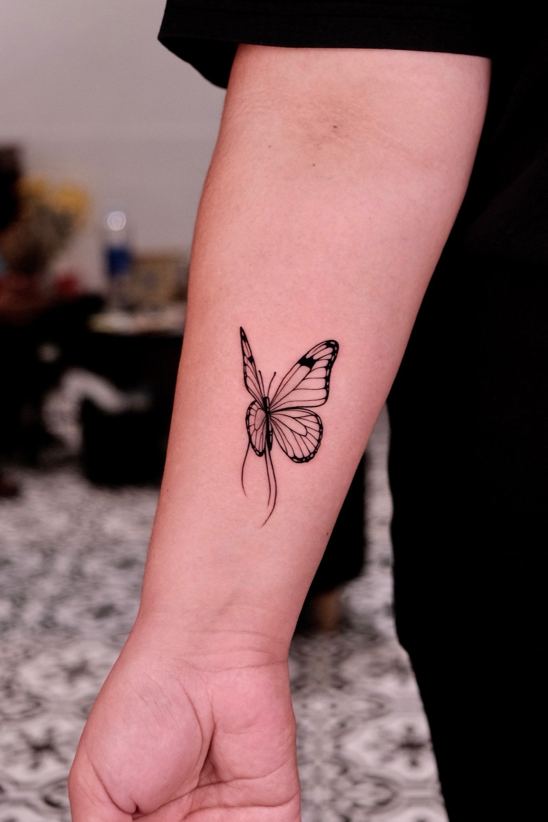 Fine-line monarch butterfly tattoo on the forearm