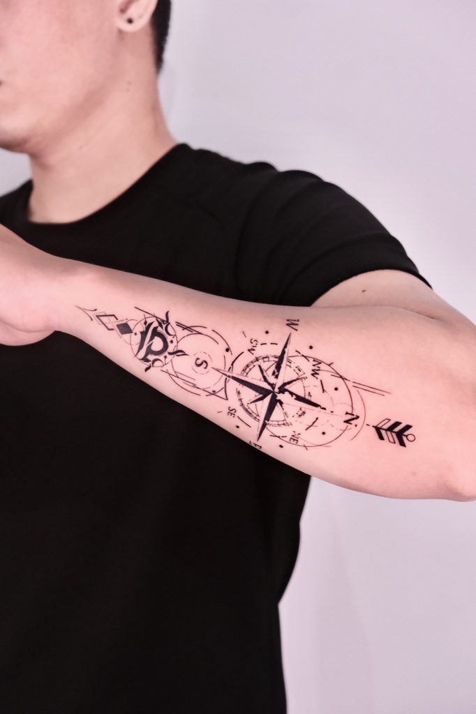 Fine-line compass with an arrow tattooed along the forearm