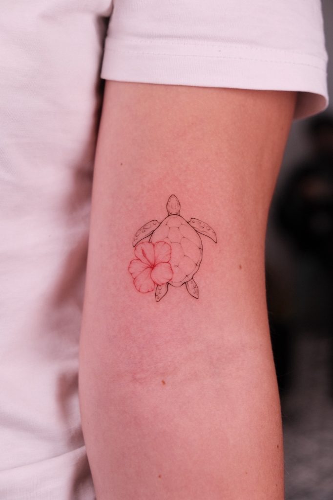Fine-line sea turtle and hibiscus flower tattoo on the upper arm