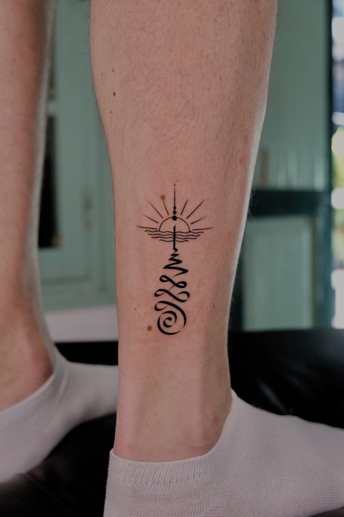 Fine-line unalome with a lotus and sun on the lower leg