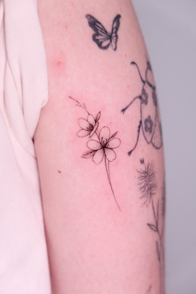 Fine-line butterfly and wildflowers tattooed along the arm