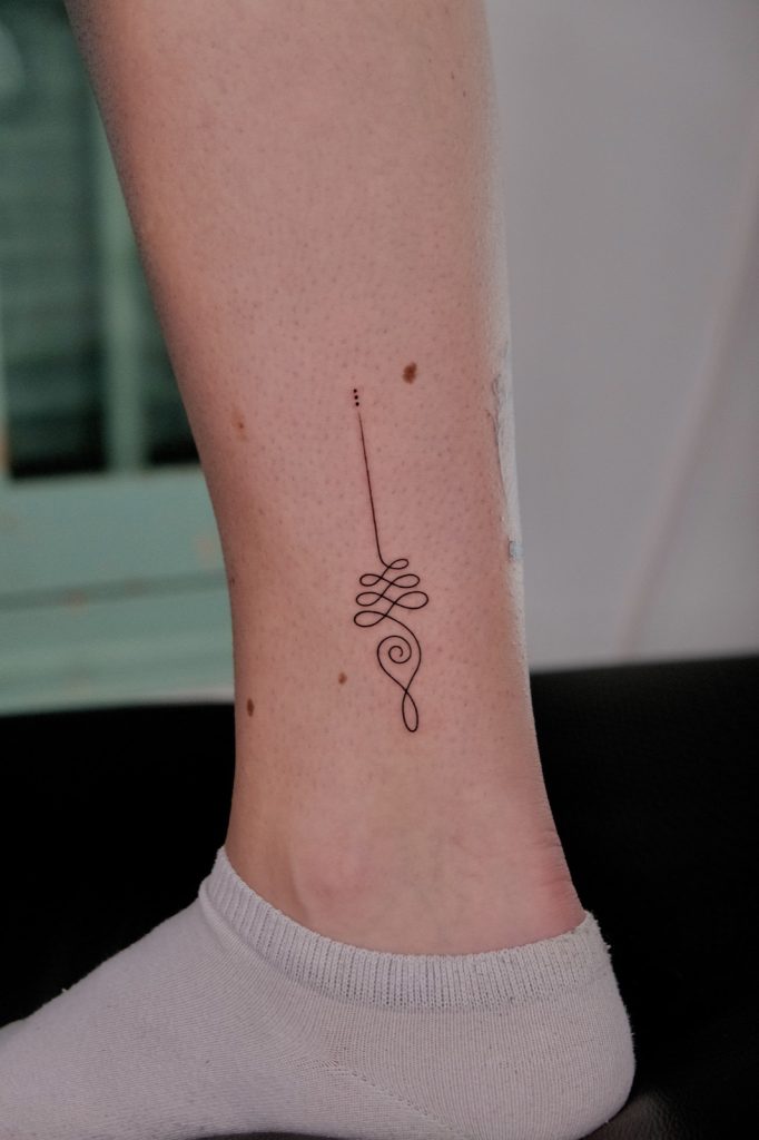 Fine-line unalome tattoo above the ankle