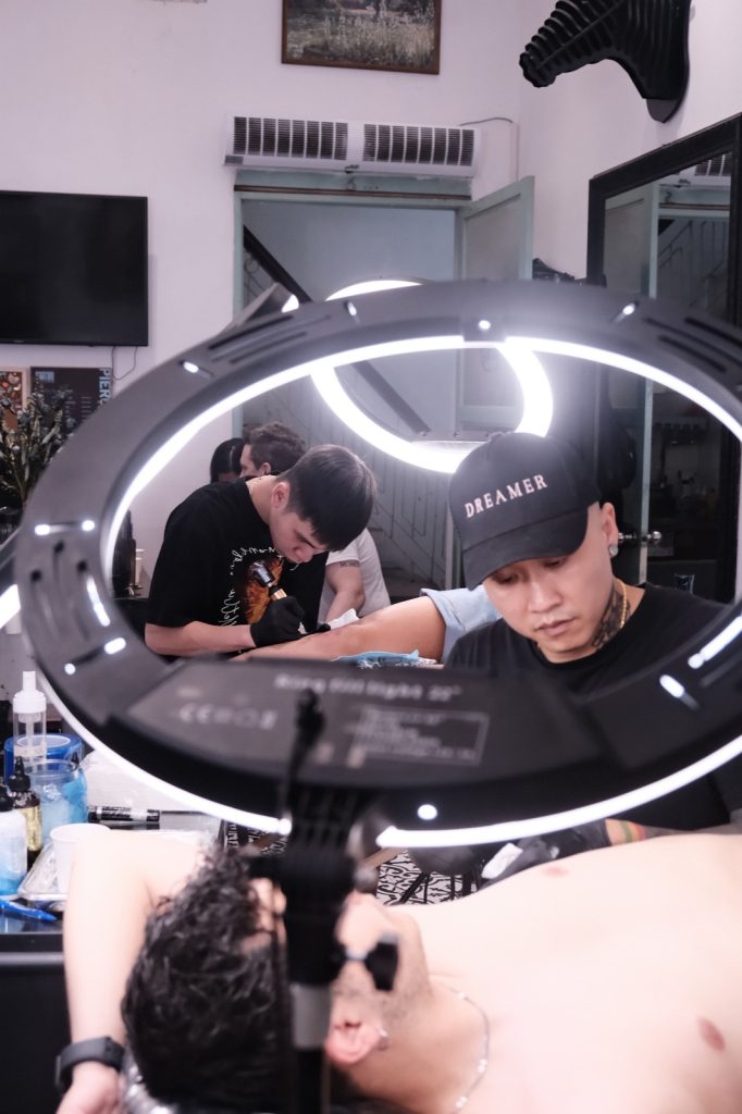 Tattoo artist working on a client lying under a ring light