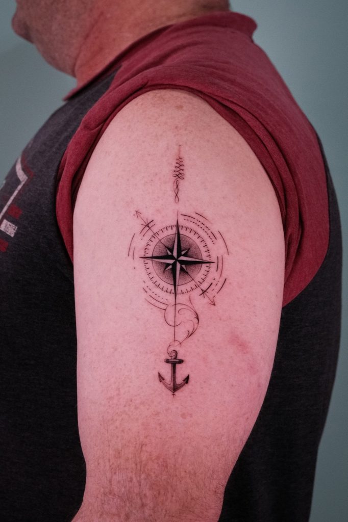 Fine-line compass with an anchor tattooed on the upper arm