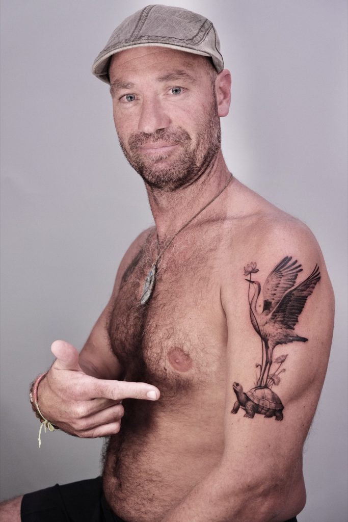 Client showing his crane-on-turtle tattoo with a lotus on the upper arm