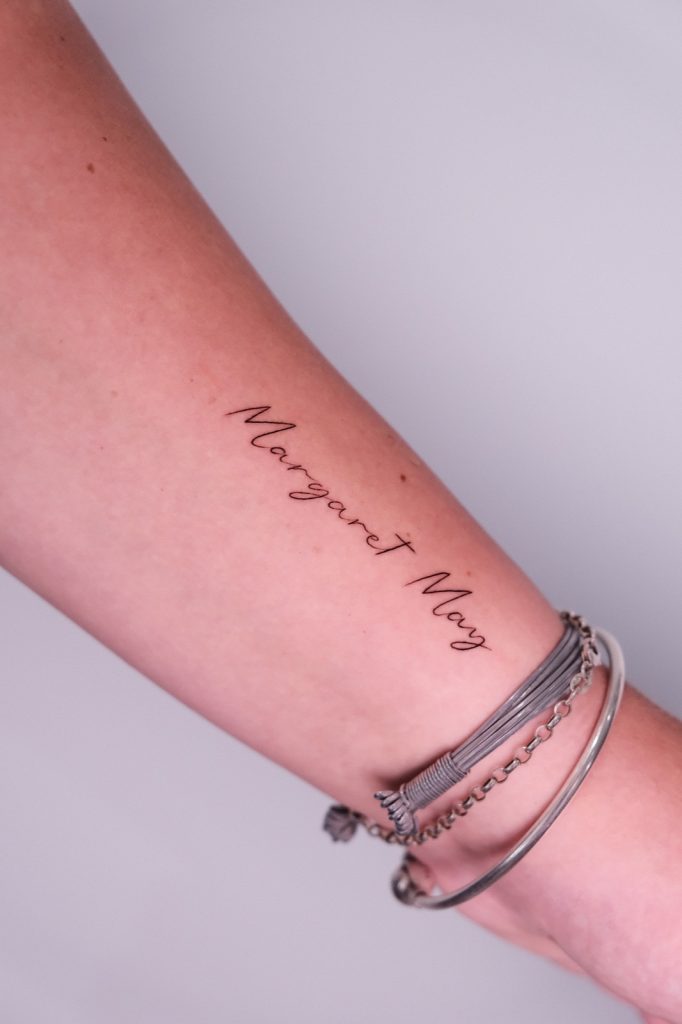 Fine-line script name tattooed along the forearm
