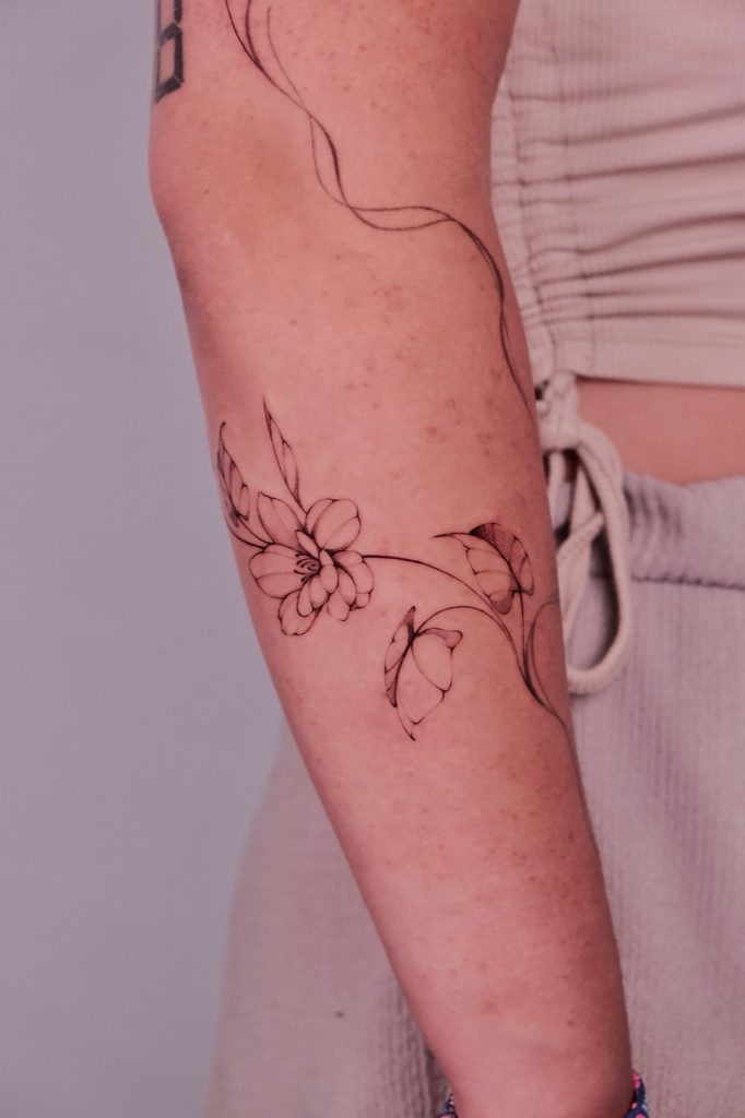 Fine-line flower vine with a small butterfly on the arm
