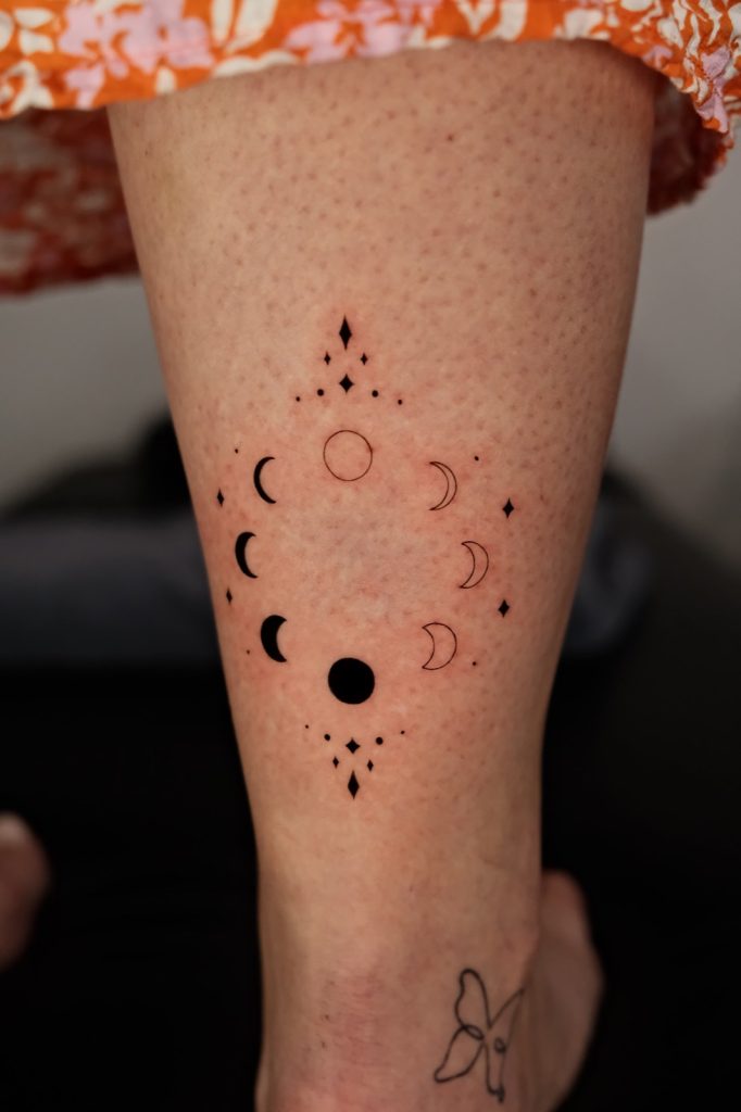 Moon phases and small dots tattooed in a circle on the back of the calf
