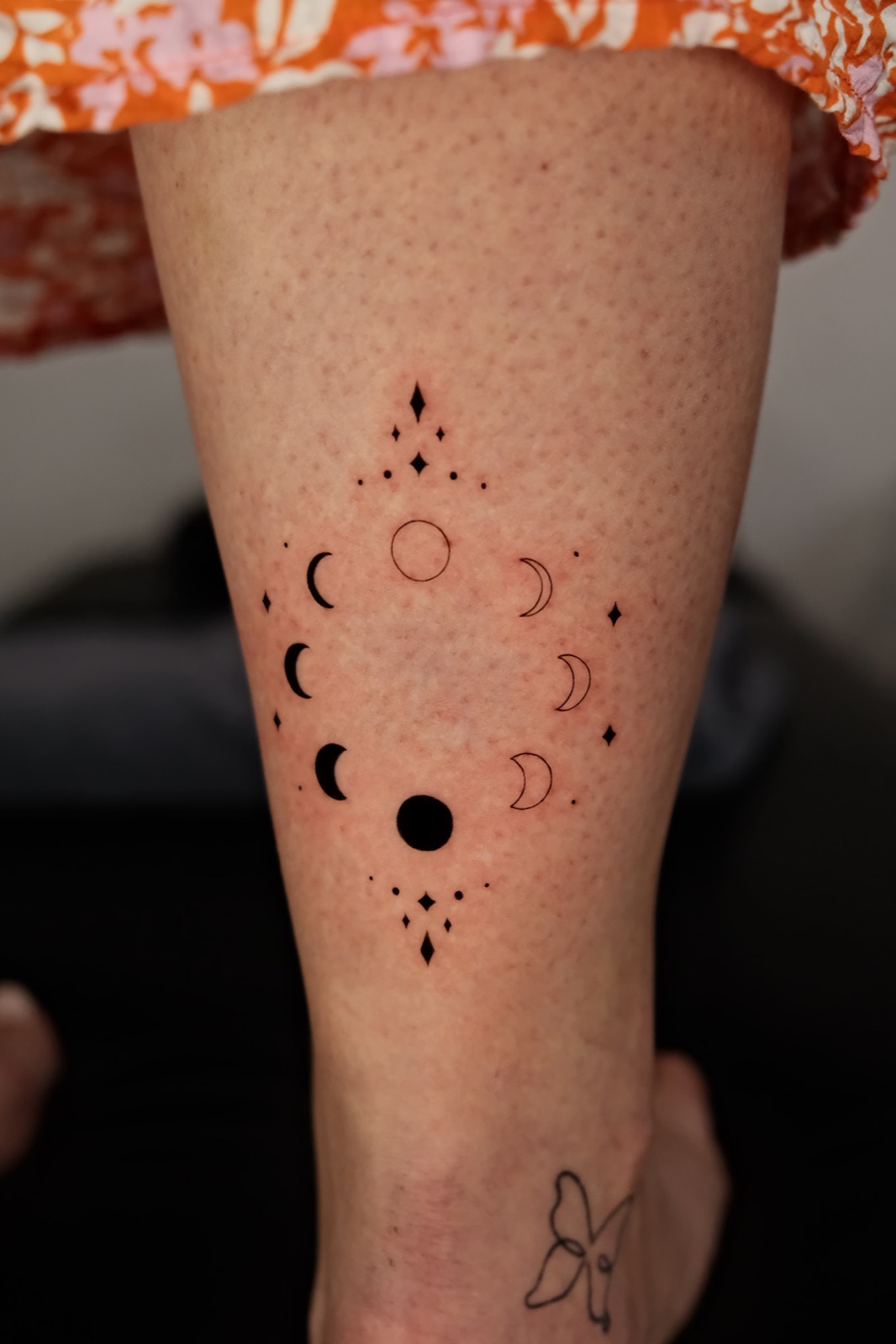 Moon phases and small dots tattooed in a circle on the back of the calf
