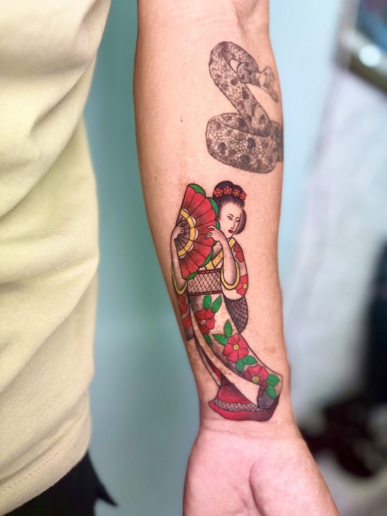 Black and grey coiled snake above a Japanese-style geisha tattoo on the forearm