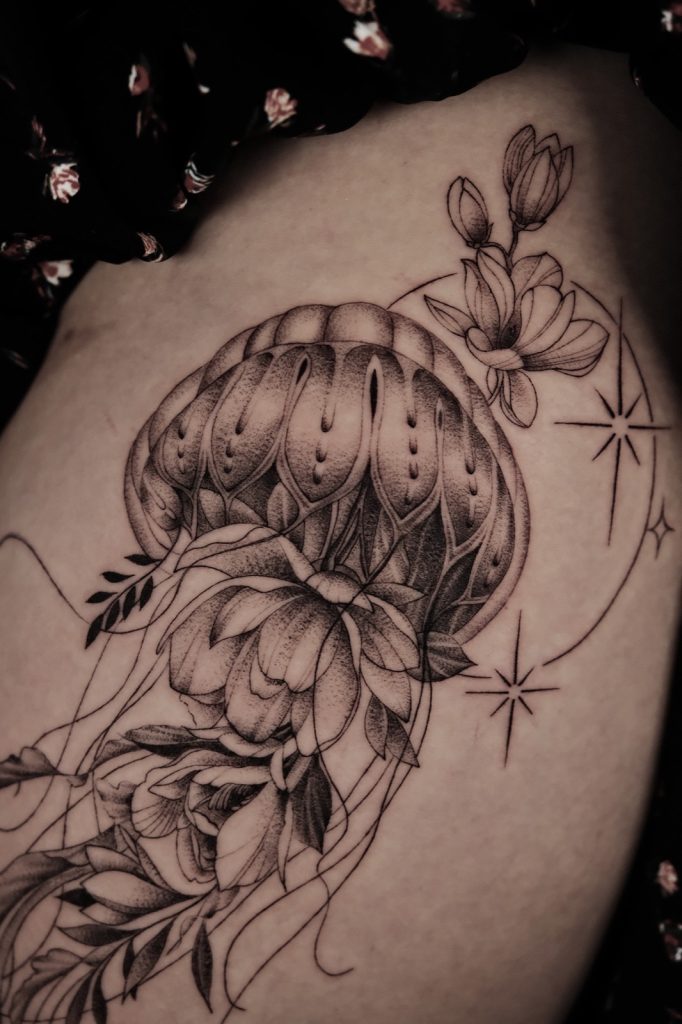 Black and grey jellyfish tattoo with flowers and stars on the hip and thigh