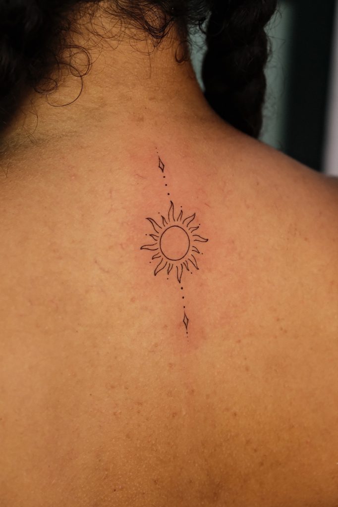 Small fine-line sun tattoo on the upper back
