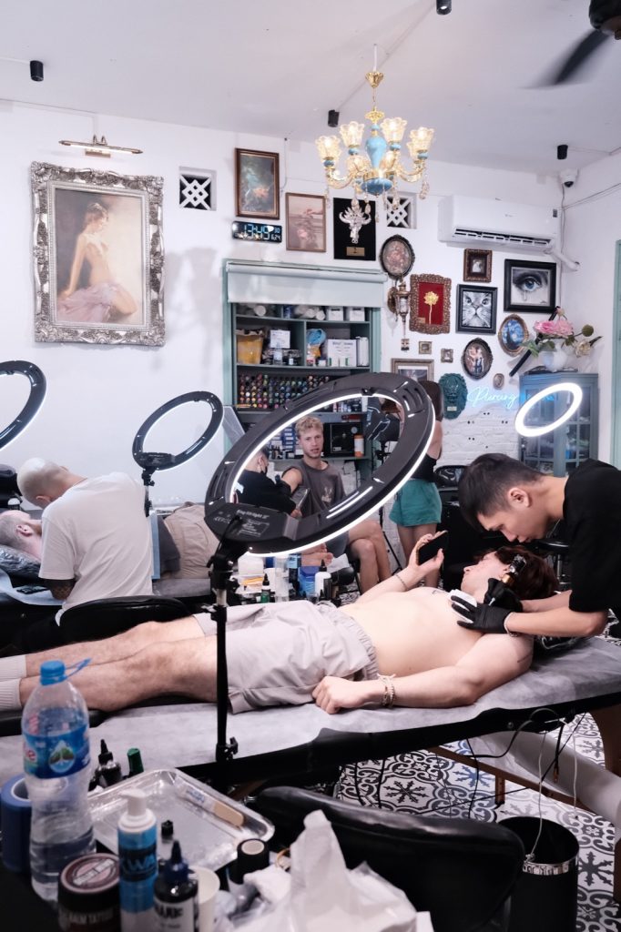 Artist tattooing a client lying on the bed in a decorated studio
