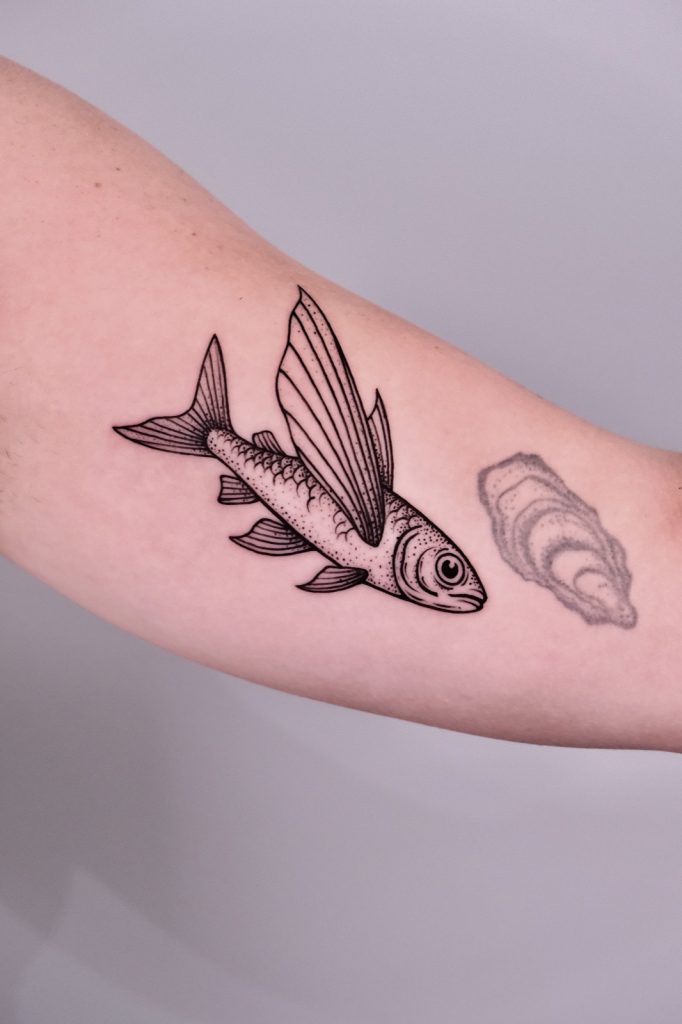 Blackwork flying fish and oyster shell tattoo on the inner arm