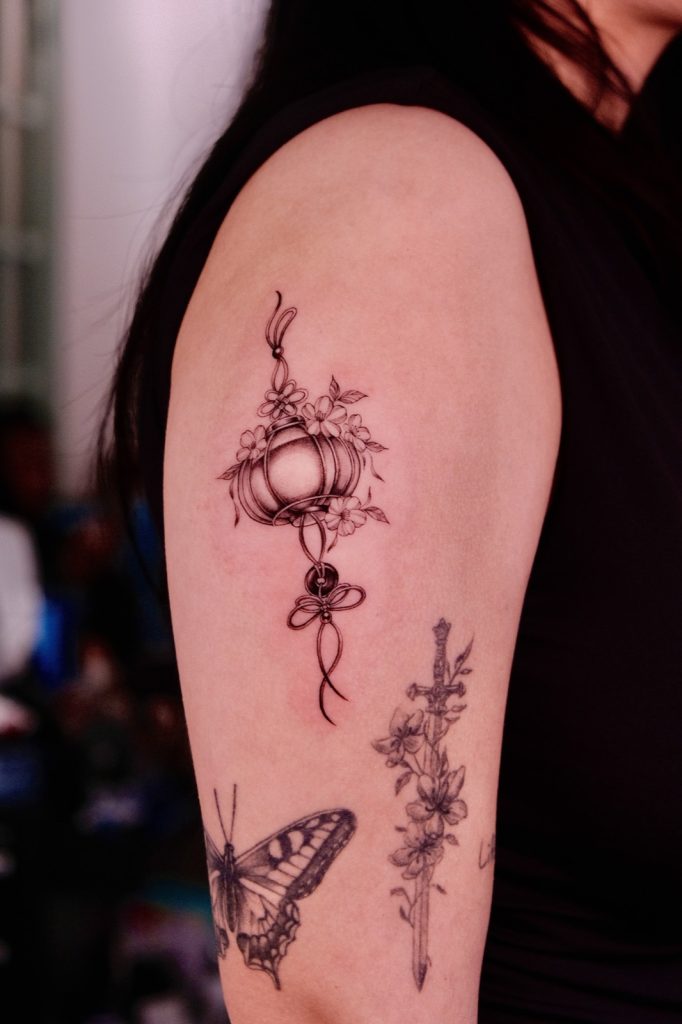 Lantern, flowers and butterfly tattoos on the upper arm