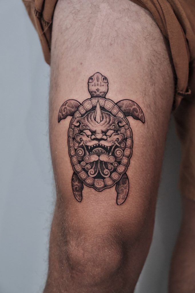 Black and grey turtle tattoo with a guardian beast face on the thigh